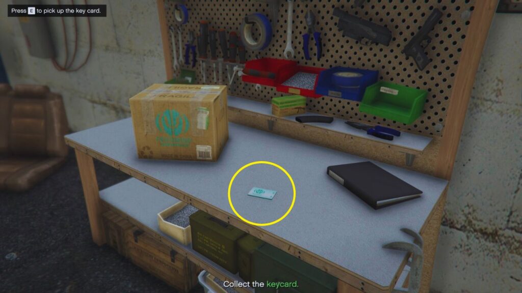 The keycard highlighted by a thin, yellow circle near a medium-sized box, a ledger, and a weapons workshop.